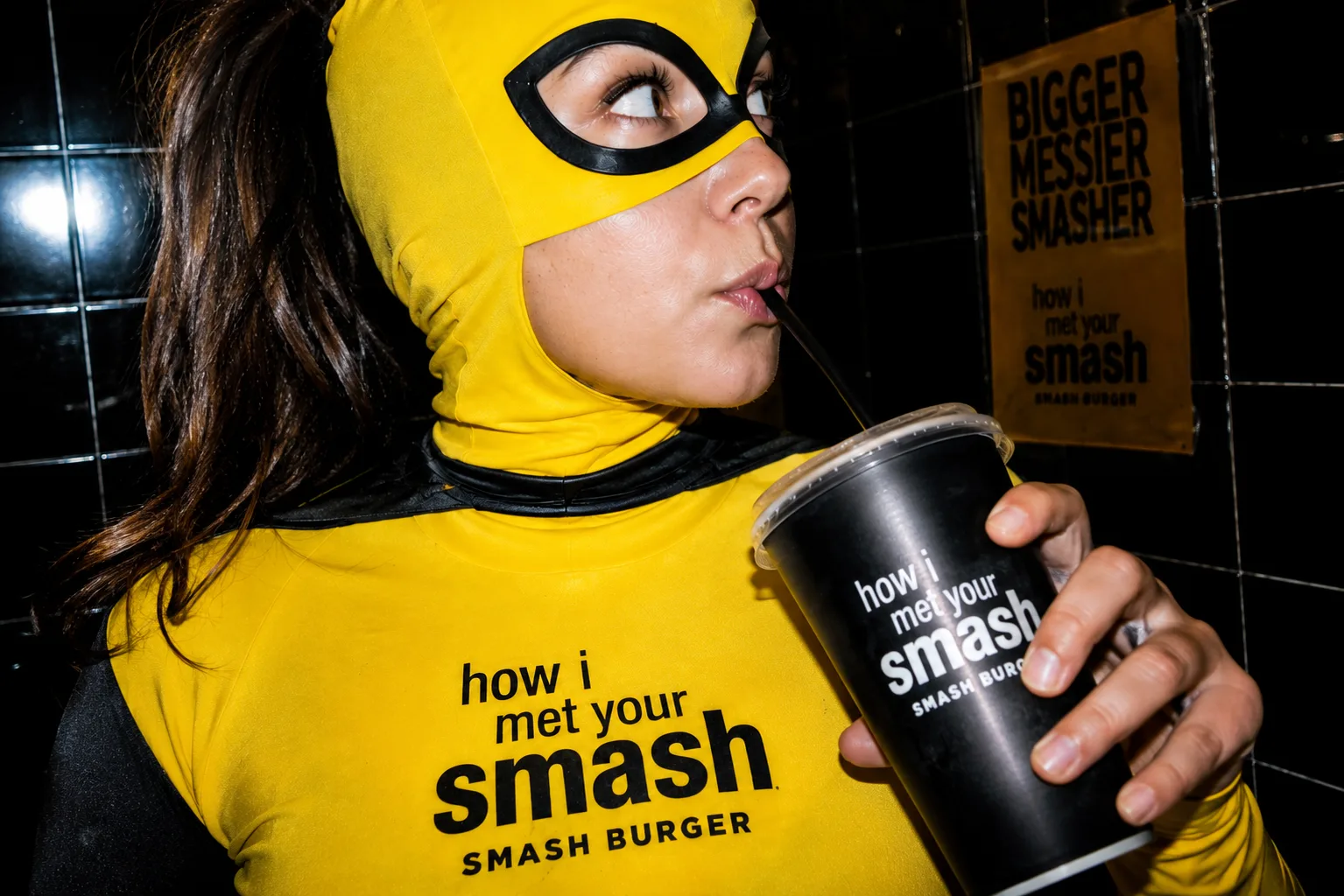 Ragazza con la maschera gialla di How I Met Your Smash che beve dal bicchiere del locale
