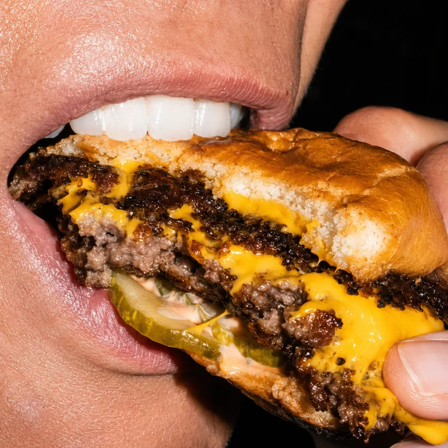 Morso di un doppio smash burger con American cheese fuso e cetriolini